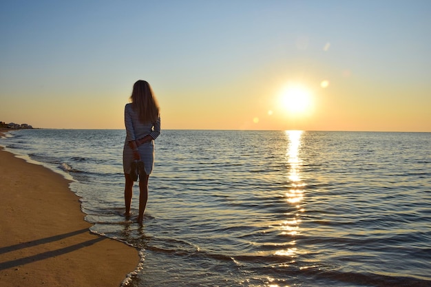 Młoda kobieta spaceruje po bezludnej plaży nad brzegiem morza, trzymając w rękach buty