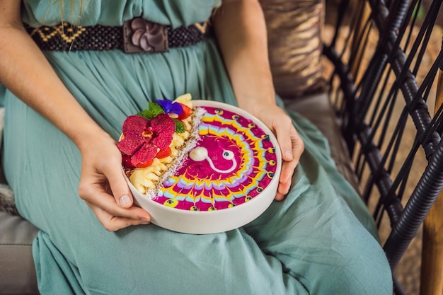 Młoda kobieta spożywająca śródziemnomorskie śniadanie siedzi przy swojej sofie i je zdrowe tropikalne śniadanie