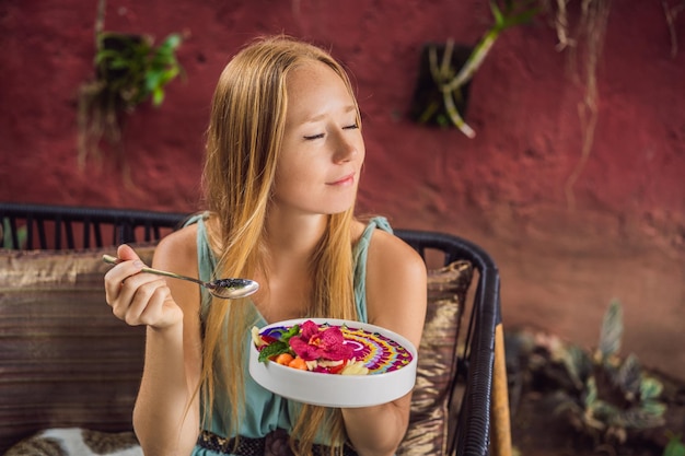 Zdjęcie młoda kobieta spożywająca śródziemnomorskie śniadanie siedzi przy swojej sofie i je zdrowe tropikalne śniadanie