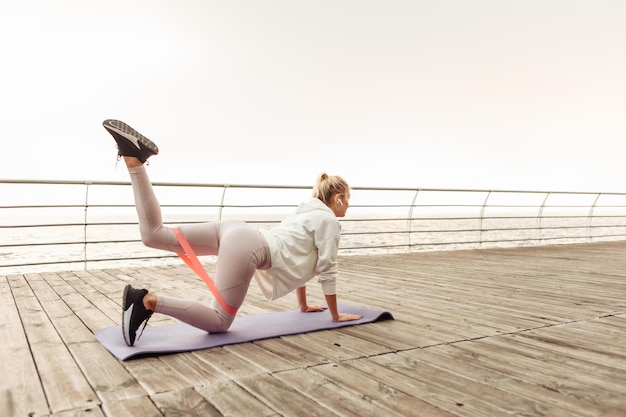 Młoda kobieta sprawny trenuje nogi z gumkami fitness na plaży. Zdrowy tryb życia