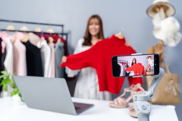 Młoda kobieta sprzedająca ubrania online za pośrednictwem transmisji na żywo przez smartfona, biznesowy e-commerce w domu