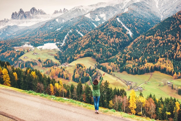 Młoda kobieta stoi na tle jesiennego lasu i gór w Dolomitach