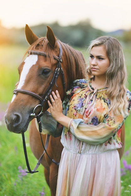 Młoda kobieta stoi obok konia w letniej sukience na łące