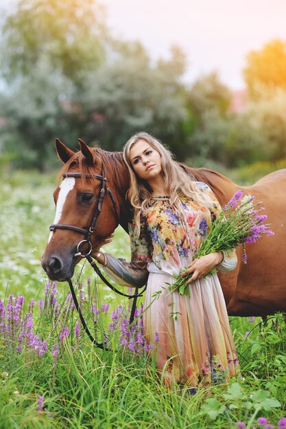 Młoda kobieta stoi obok konia w letniej sukience na łące