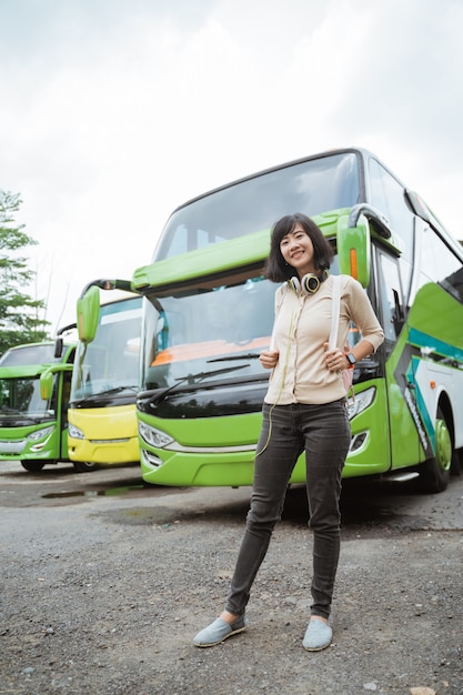 Młoda kobieta stoi w plecaku i słuchawkach uśmiechając się na tle autobusu