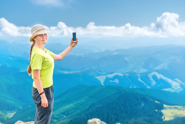 Młoda kobieta stojąca na klifie góry i biorąca selfie z podróży na smartfonie