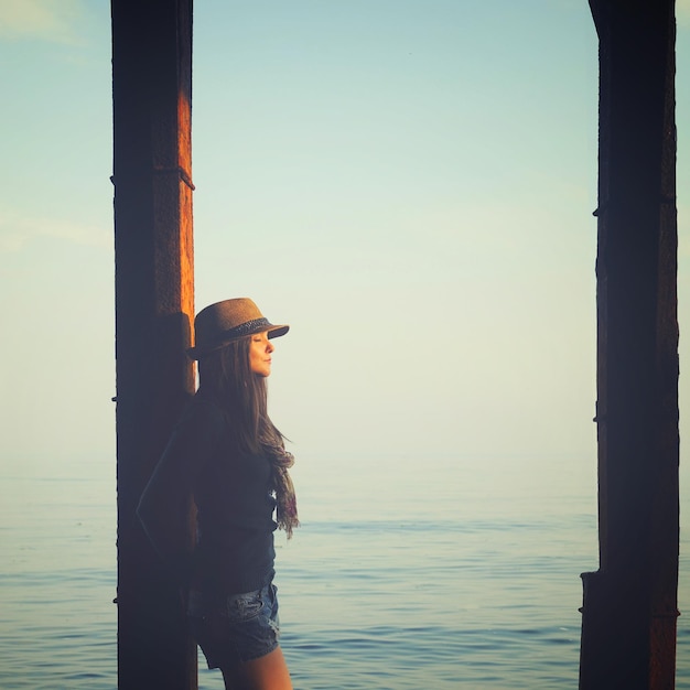 Młoda kobieta stojąca pod molo w morskiej wodzie, ciesz się jesiennym światłem zachodu słońca i zrelaksuj się