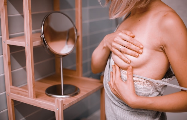 Zdjęcie młoda kobieta stojąca przed lustrem, sprawdzająca piersi podczas samooceny. świadomość raka piersi. jak sprawdzić koncepcję piersi.