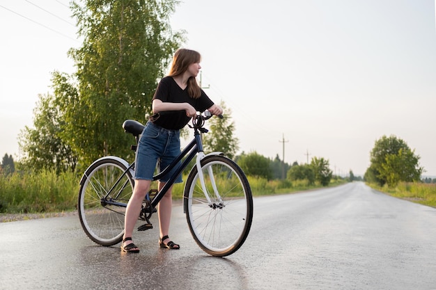 Zdjęcie młoda kobieta stojąca samotnie na drodze z rowerem na wsi letnia aktywność zdrowy styl życia