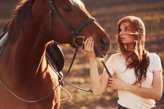 Młoda kobieta stojąca z koniem w polu rolnictwa w słoneczny dzień