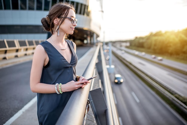 Młoda kobieta stojąca z telefonem na autostradzie podczas podróży służbowej