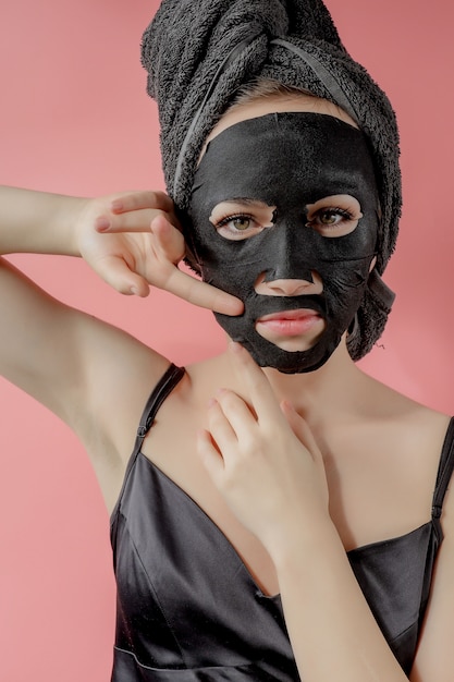 Młoda kobieta stosuje czarną maseczkę kosmetyczną na różowej ścianie. Maska peelingująca z węglem drzewnym, zabiegi kosmetyczne w spa, pielęgnacja skóry, kosmetologia. Ścieśniać