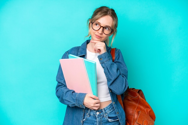 Młoda kobieta student na białym tle na niebieskim tle i patrząc w górę