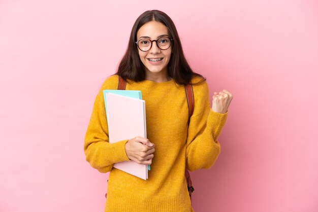 Młoda kobieta student na białym tle świętuje zwycięstwo w pozycji zwycięzcy