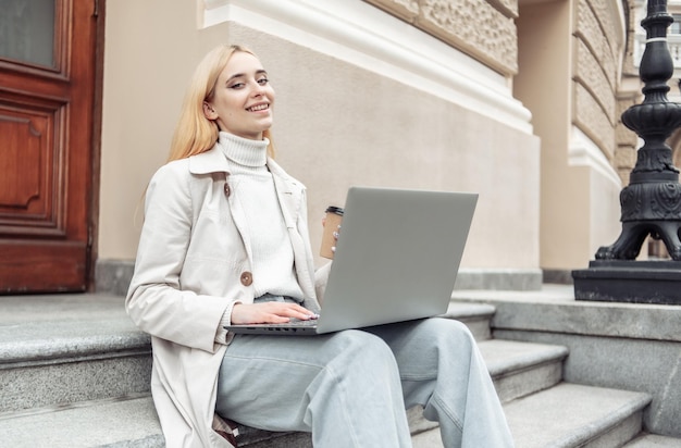 Młoda kobieta student używa laptopa siedząc na schodach w mieście