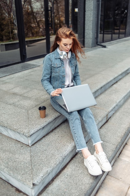 Młoda kobieta studentka lub freelancer siedzi na schodach z laptopem