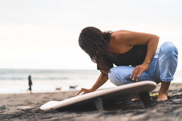 Młoda kobieta surfer przygotowuje deskę surfingową na oceanie, woskowanie Kobieta z deską surfingową na oceanie aktywny styl życia sporty wodne