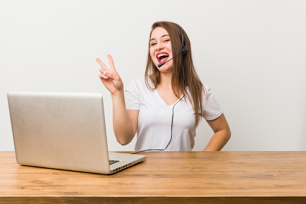 Młoda kobieta telemarketer radosny i beztroski, pokazując symbol pokoju palcami.