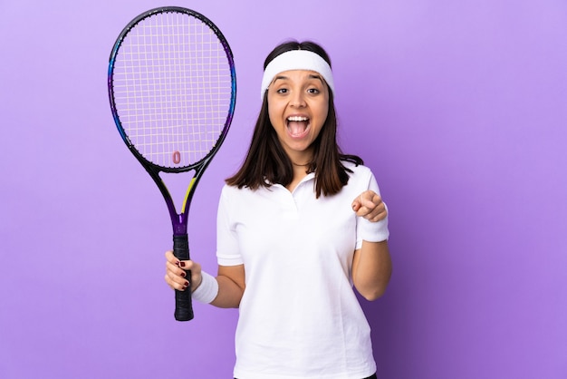 Młoda kobieta tenisista na białym tle zaskoczony i wskazujący przód
