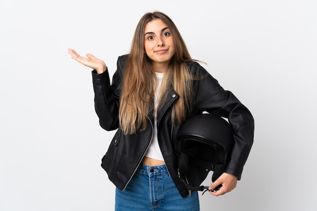Młoda kobieta trzyma motocyklowego hełm nad odosobnioną biel ścianą ma wątpliwości z zmieszanym twarzy wyrażeniem