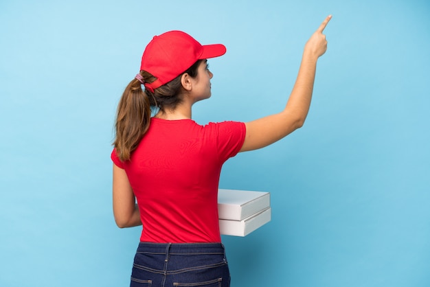 Młoda kobieta trzyma pizzę nad odosobnioną menchii ścianą wskazuje z powrotem z palcem wskazującym