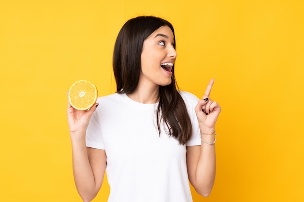 Młoda kobieta trzyma pomarańcze odizolowywająca na kolor żółty ścianie zamierza realizować rozwiązanie podczas gdy podnoszący palec up