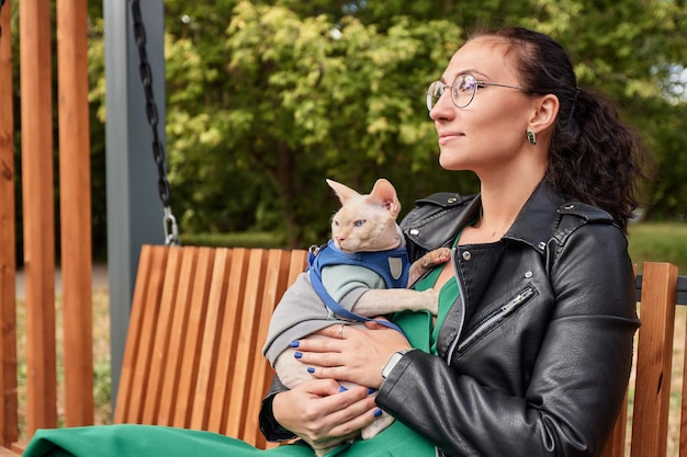 Młoda kobieta trzyma swojego kota w amoveralls na nogach Kot na spacerze Miłość do zwierząt Zbliżenie