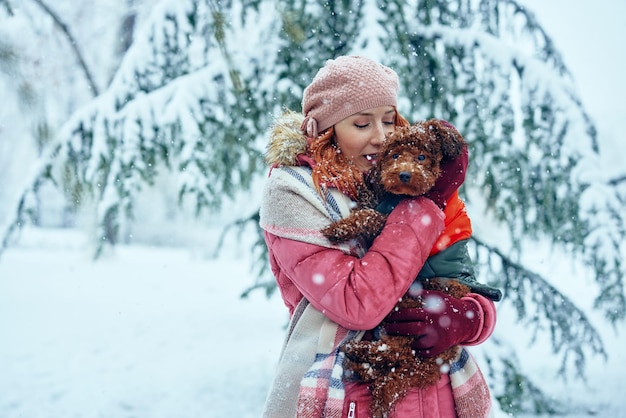 Młoda kobieta trzyma swojego uroczego szczeniaka i cieszy się razem zimowym dniem na świeżym powietrzu