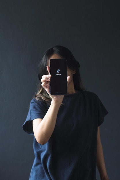 Młoda kobieta trzyma telefon z logo Tiktok na ekranie. Koncepcja młodzieży, technologii, społeczności i