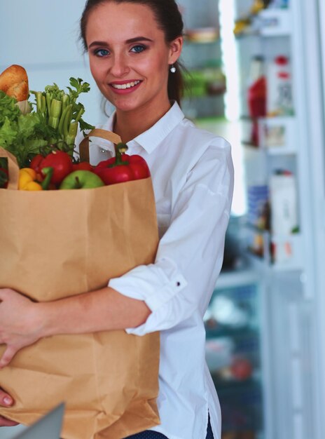 Młoda kobieta trzyma torbę na zakupy spożywcze z warzywami stojącymi w kuchni