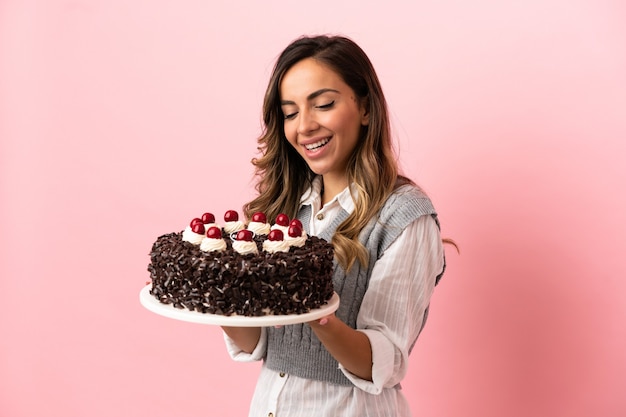 Młoda kobieta trzyma tort urodzinowy na odosobnionym różowym tle