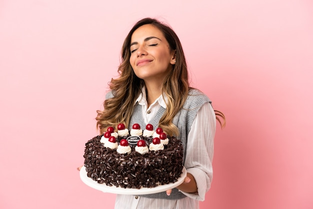 Młoda kobieta trzyma tort urodzinowy na odosobnionym różowym tle