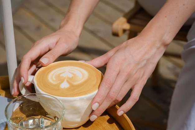 Młoda kobieta trzyma w dłoniach filiżankę świeżo zaparzonej pysznej i pachnącej porannej kawy cappuccino