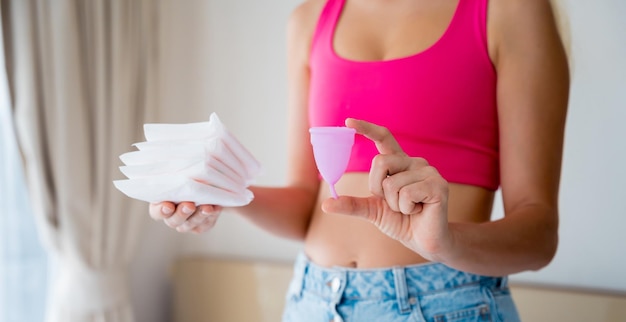 Młoda kobieta trzyma w dłoniach kubeczek menstruacyjny i podpaski