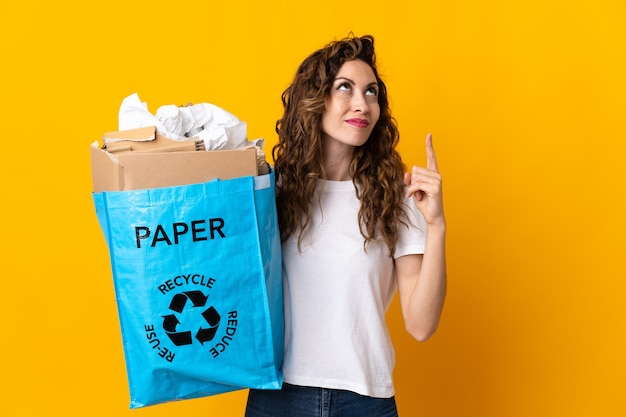 Młoda kobieta trzyma worek recyklingu pełnego papieru do recyklingu na żółtym, wskazując na świetny pomysł