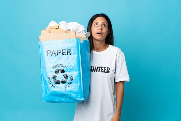 Młoda kobieta trzyma worek recyklingu pełnego papieru, patrząc w górę iz zaskoczonym wyrazem twarzy