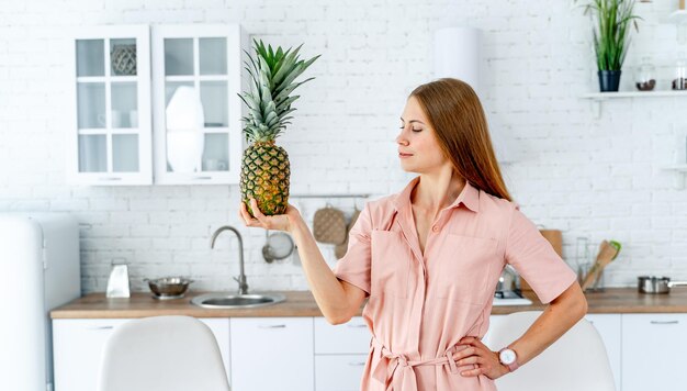Młoda kobieta trzymająca ananas w kuchni Młoda kobietą trzymającą ananas w kuchenie