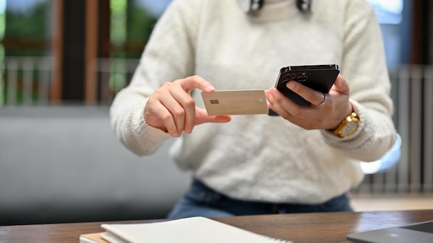 Młoda kobieta trzymająca kartę kredytową i smartfon korzystający z bankowości mobilnej lub bankowości internetowej