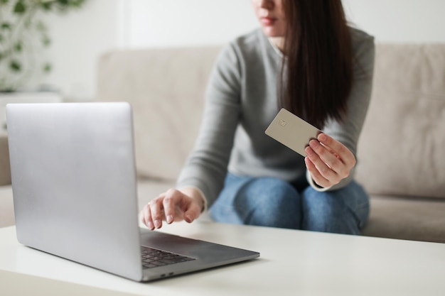 Młoda kobieta trzymająca kartę kredytową i używająca laptopa w domu, płacąc online zakupy domowe bankowość internetowa