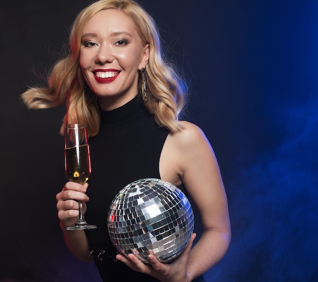 Młoda kobieta trzymająca kieliszek wina i kula dyskotekowa w klubie nocnym