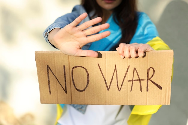 Zdjęcie młoda kobieta trzymająca plakat ze słowami no war i pokazująca gest zatrzymania w pobliżu lekkiej ściany zbliżenie