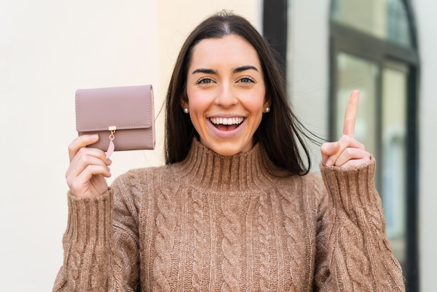 Młoda kobieta trzymająca portfel na zewnątrz, wskazująca na świetny pomysł
