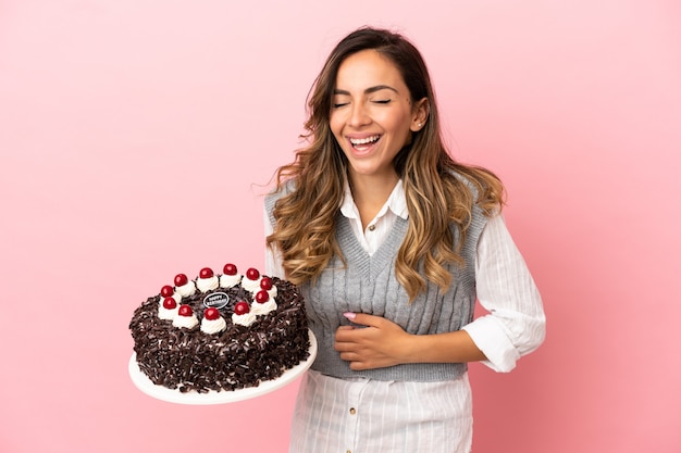 Młoda kobieta trzymająca tort urodzinowy na odosobnionym różowym tle często się uśmiecha