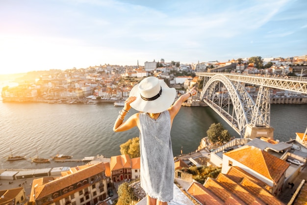 Młoda kobieta turysta, ciesząc się pięknym widokiem krajobrazu na stare miasto z rzeką i słynnym żelaznym mostem podczas zachodu słońca w mieście Porto, Portugalia