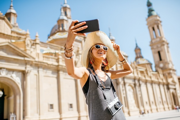 Młoda kobieta turysta co selfie zdjęcie przed słynną katedrą na centralnym placu podczas słonecznej pogody w mieście Saragossa, Hiszpania