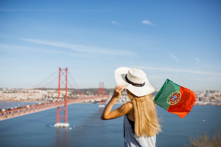 Zdjęcie młoda kobieta turysta podziwiająca piękny widok z lotu ptaka na słynny żelazny most siedzący z portugalską flagą w mieście lizbona, portugalia