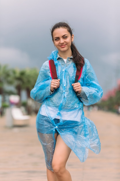 Zdjęcie młoda kobieta turysta w płaszczu z plecakiem, uśmiechając się i patrząc w kamerę