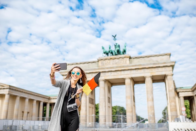 Zdjęcie młoda kobieta turystka robiąca zdjęcie selfie z niemiecką flagą stojącą przed słynną bramą brandenburską w berlinie