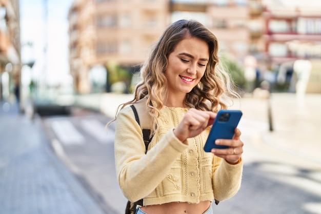 Młoda kobieta turystka uśmiecha się pewnie za pomocą smartfona na ulicy