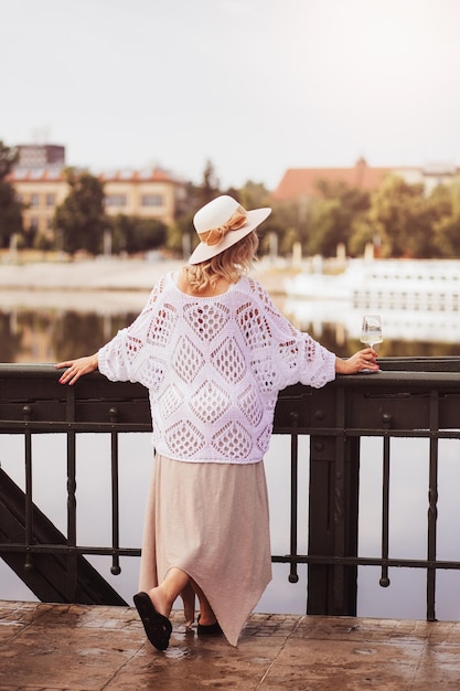 Młoda kobieta turystyczna stojąca z kieliszkiem białego wina na moście w europejskim mieście rzeka w tle